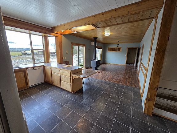Open floor plan, kitchen in the foreground, dining room living room on the other side of the wood stove. Bedroom 1 and Bedroom 2 lead off this room to the left and the master bedroom is through the far door.