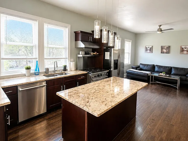 Open kitchen with large granite island, stainless appliances, and generous cabinet storage, flowing into the living area.