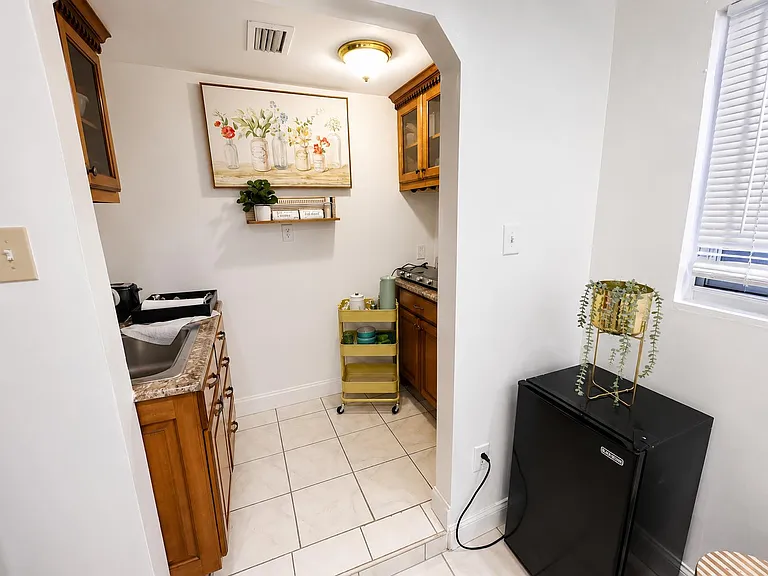 Compact kitchen nook with wood cabinetry, tiled floors, and an extra mini-fridge for convenient food and drink storage.