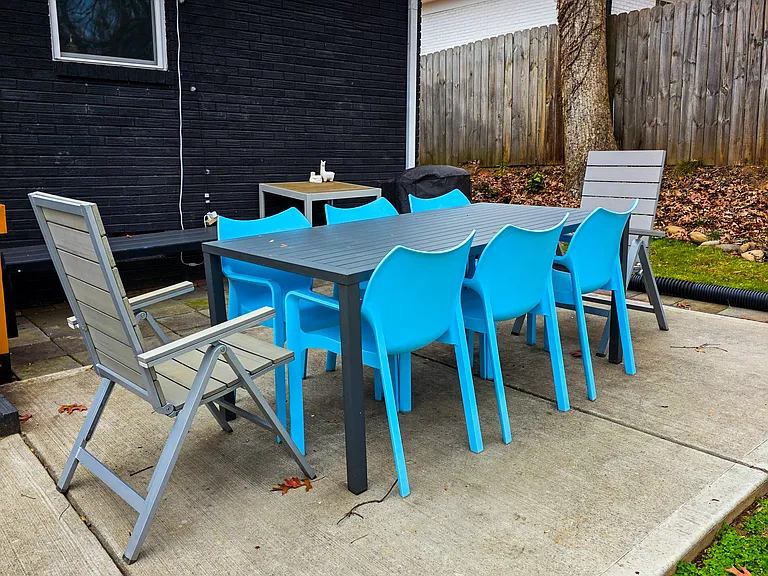 Outdoor dining area including a large table and seating, and an additional bench and table. The patio also features a wood pellet smoker/grill and string lights.