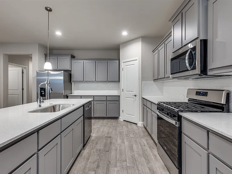 Kitchen with gray cabinetry, pendant lighting, light hardwood / wood-style flooring, stainless steel appliances, and sink