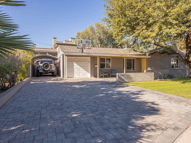 Large paver driveway with covered carport, offering shaded parking and a thoughtfully maintained entry