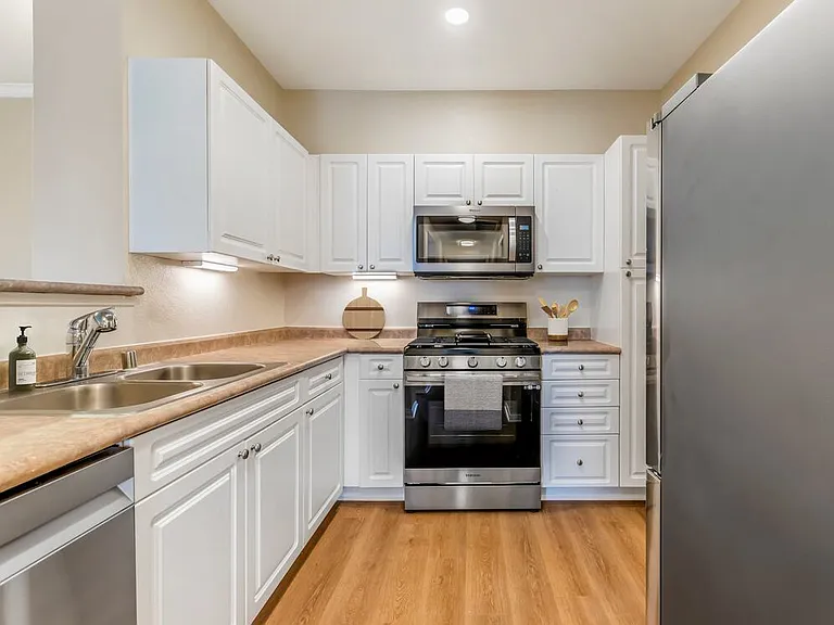 Renovated Package I kitchen with upgraded stainless steel appliances, white cabinetry, neutral laminate countertops, and upgraded hard surface flooring