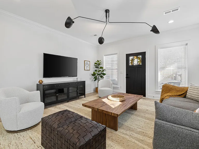 Comfortable living room with ample seating, a wall-mounted TV, and large windows with blinds for adjustable privacy.