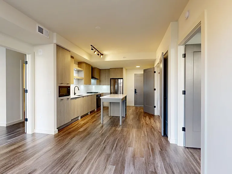 Apartment kitchen with black stainless steel appliances, dining and living room with wood-style flooring.