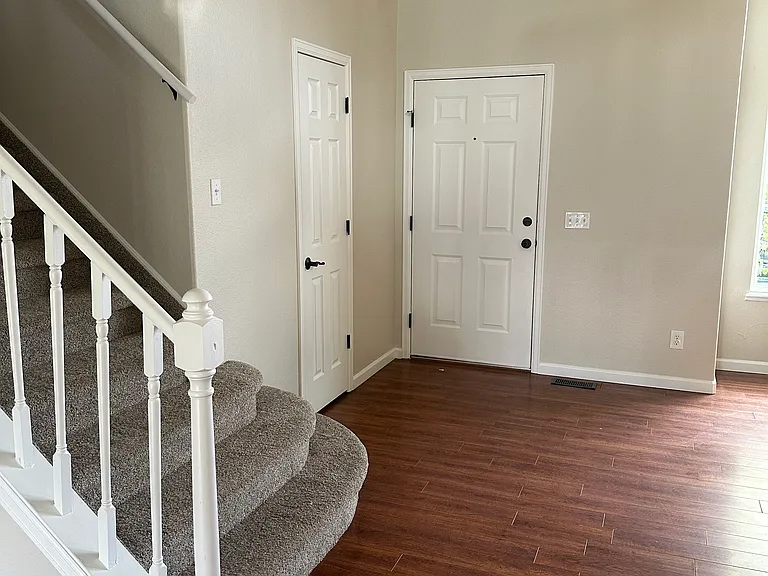View of front door, coat closet, and staircase taken from kitchen.