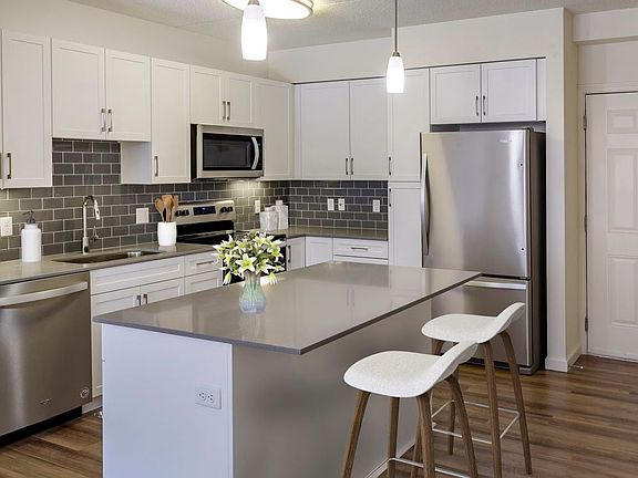 Renovated Package II kitchen with grey quartz countertops, white shaker cabinetry, stainless steel appliances, grey tile backsplash, and hard surface flooring throughout