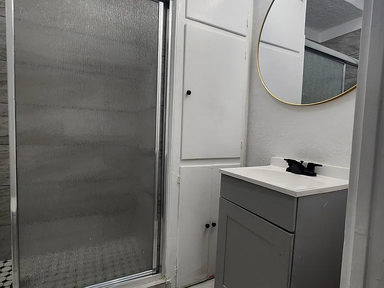 Bathroom includes a walk-in shower with sliding glass doors, a single-sink vanity, and a framed mirror with overhead lighting