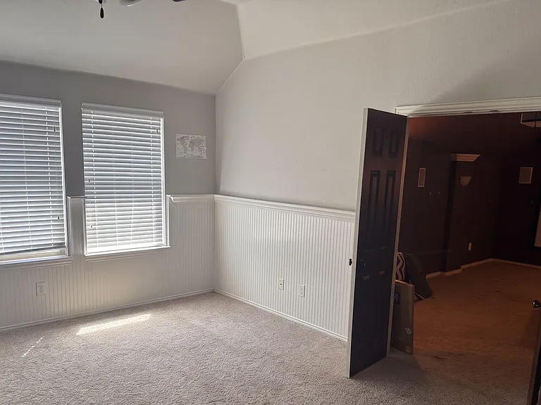 Spacious carpeted room with three windows, white wainscoting, and neutral walls offering flexible layout options.