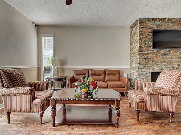 Charming living room with a cozy leather sofa, striped armchairs, and a stone fireplace, perfect for relaxation and entertainment.