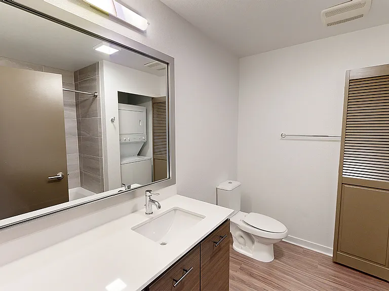 Apartment bathroom with wood-style flooring and in-home washer and dryer.
