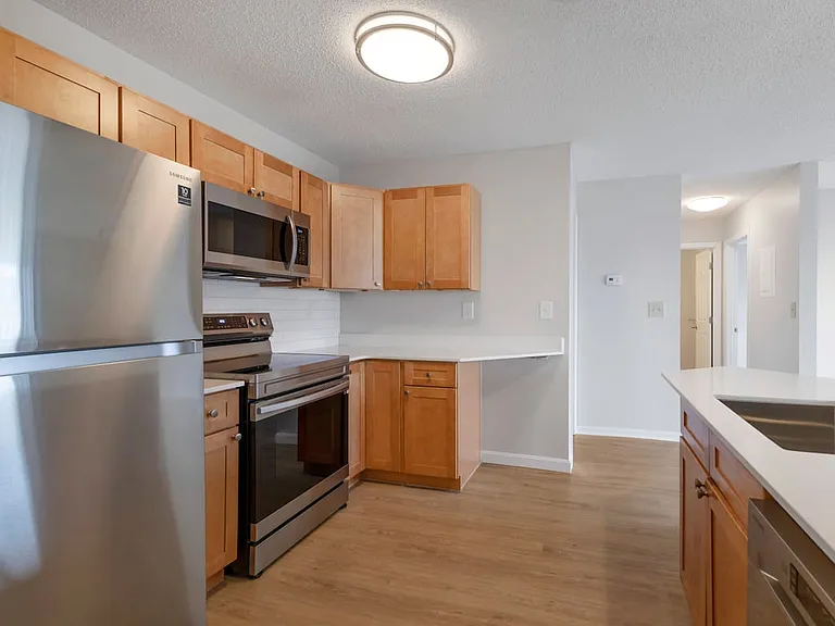 Renovated Package I kitchen with stainless steel appliances, white quartz countertops, maple cabinetry, white tile backsplash, and hard surface flooring