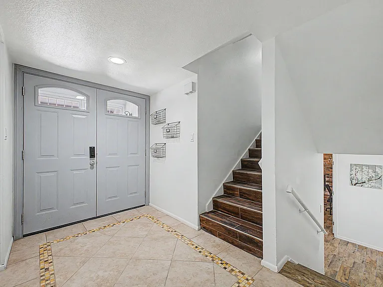 Welcoming tiled entry foyer with double doors, staircase access, and wall-mounted basket storage for daily essentials.