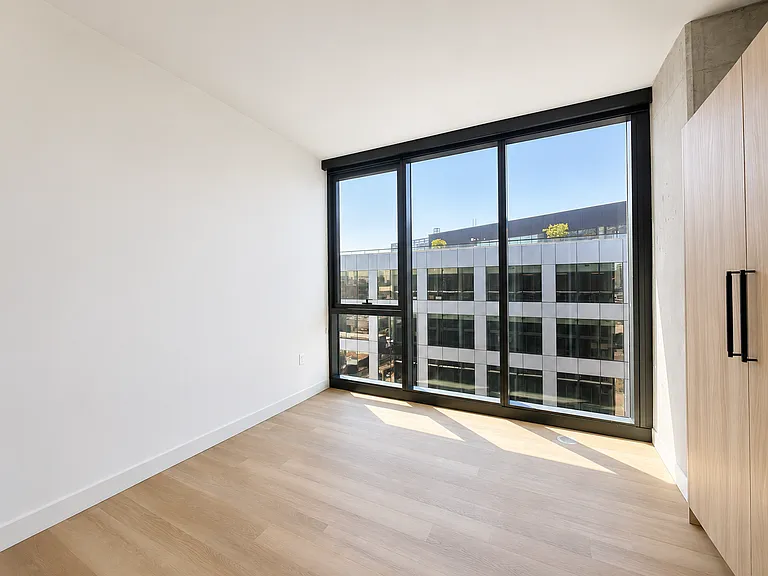 Primary bedroom at Stead 220 in Fulton Market featuring floor-to-ceiling windows with city views, a built-in Italian wardrobe closet, wide-plank flooring, and abundant natural light.