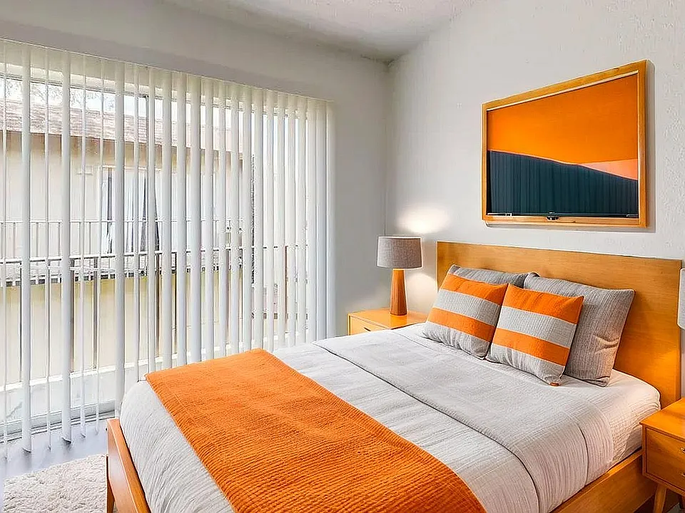 Bright and modern bedroom with floor-to-ceiling windows, vibrant orange accents, and stylish wooden furniture.