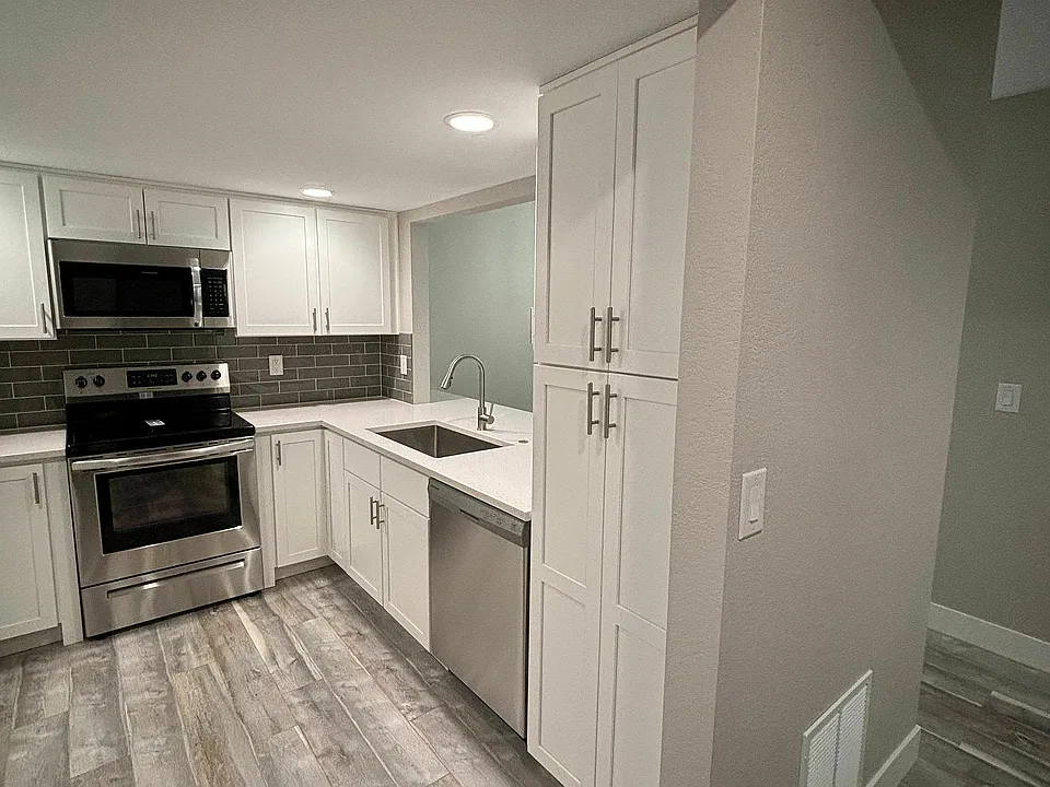Modern kitchen with sleek stainless steel appliances, elegant white cabinetry, and stylish wood flooring.