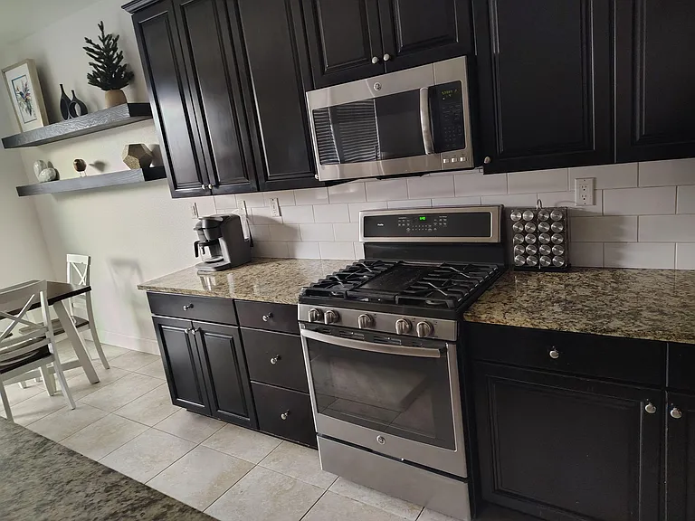 Kitchen features dark cabinetry, granite counters, subway-tile backsplash, and stainless range with over-the-range microwave.