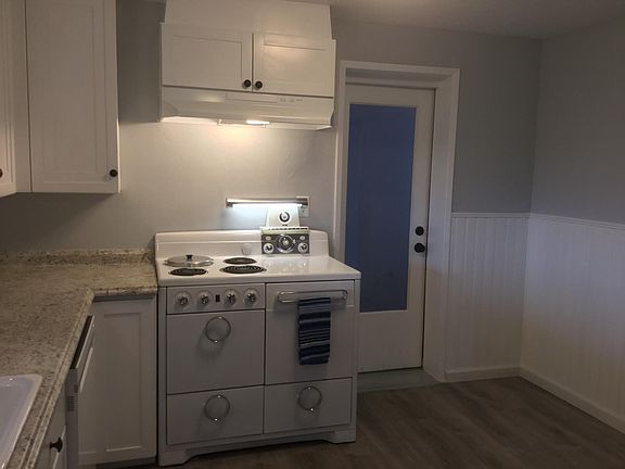 Additional view of stove with light on and cooking vent above. Door to the right of the stove goes to the garage with parking for one car and additional storage. Old fashioned bead board throughout kitchen.