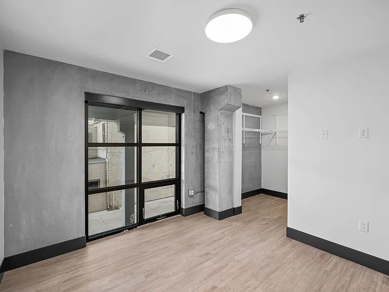 Modern apartment interior with stylish concrete accents, large glass sliding door, and built-in closet, offering a bright and open living space. Modern apartment interior with stylish concrete accents, large glass sliding door, and built-in closet, offeri