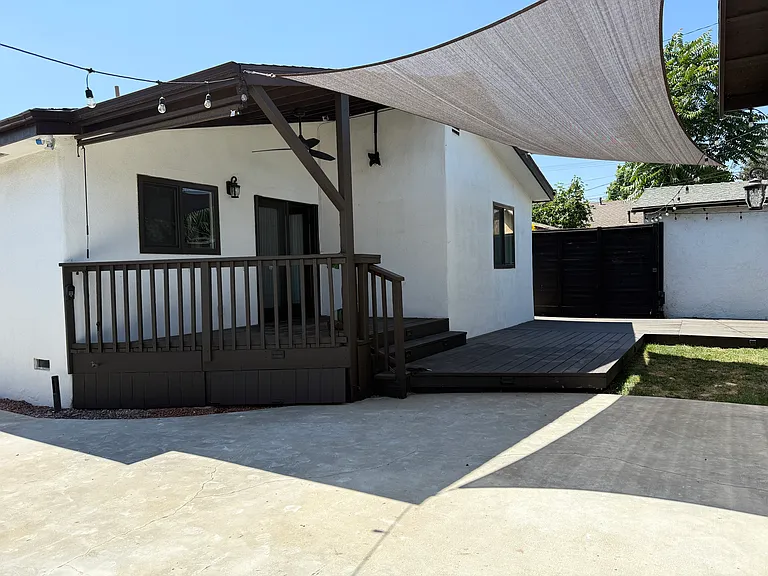 Covered backyard patio with a TV mount, Sunbrella shade, and string lighting.