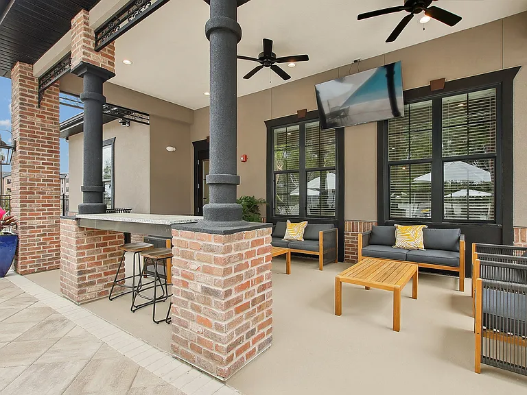 Charming outdoor patio with cozy seating, stylish brick pillars, and a wall-mounted TV, perfect for relaxation and entertaining.
