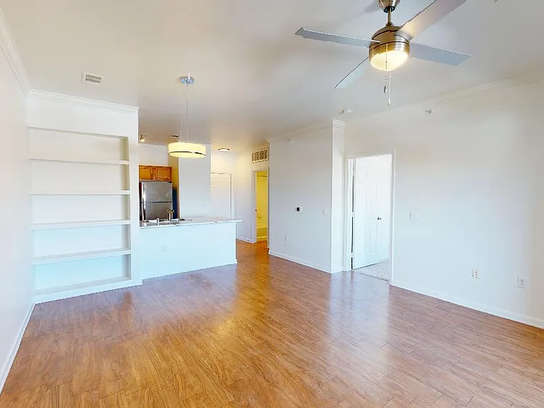 Apartment kitchen with stainless steel appliances, dining and living room with wood-style flooring.