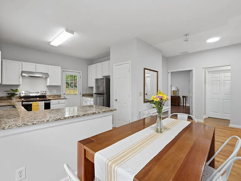 Open kitchen with granite counters, ample white cabinetry, and stainless appliances, plus an adjacent dining area.