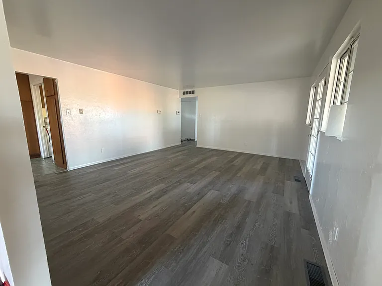 The large living room features new vinyl flooring, that is spacious enough for 3 large sofas, with entry to the backyard. Point of view from the dining room entry.