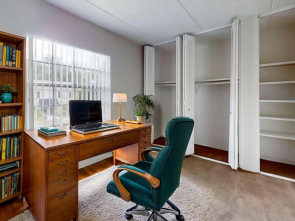 Bright home office featuring a wooden desk with a laptop, stylish green chair, bookshelf filled with books, and spacious closets, ideal for productive work from home days.