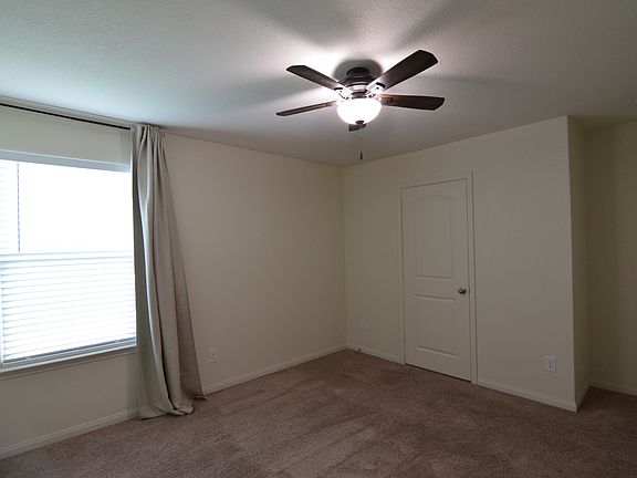 Spacious primary bedroom with natural light, ceiling fan, and installed window coverings for added comfort and privacy.