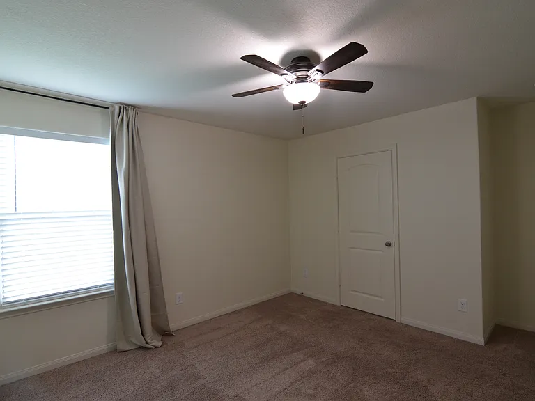 Spacious primary bedroom with natural light, ceiling fan, and installed window coverings for added comfort and privacy.