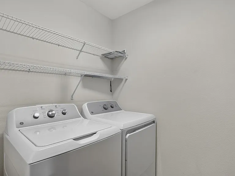 Dedicated laundry area with washer and dryer plus wire shelving for convenient storage and supplies.