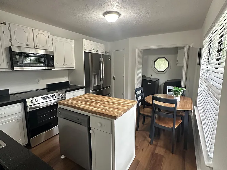 Functional kitchen with hidden washer/dryer space, stainless appliances, butcher-block island, and a dine-in breakfast nook.