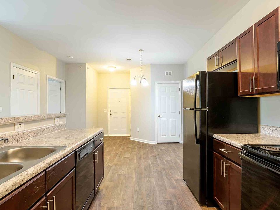 Open-concept kitchen with breakfast bar, double sink, and view into dining and entry area, finished with wood-style flooring at Cedar Terrace Apartments.
