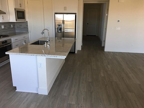 Kitchen with adjoining living room (to right in photo). Light and bright from full windows. Hallway leads to front door, garage, downstairs bedroom and full bath.