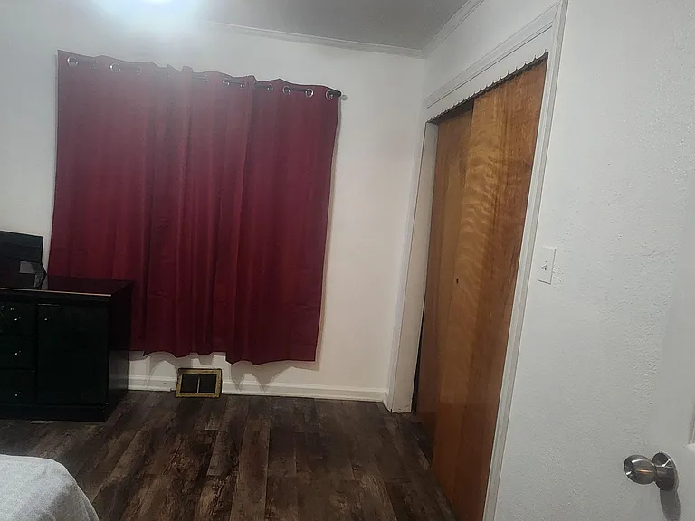 Bedroom with wood-look flooring, a window with curtain panels, and a closet for everyday storage.