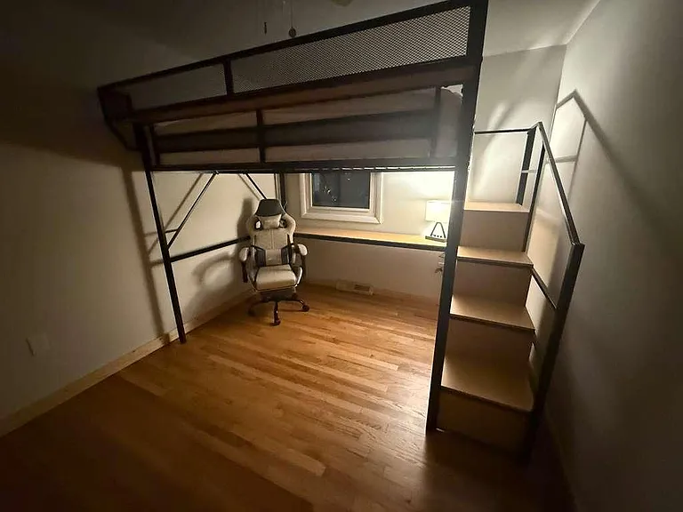 Loft-style bedroom with hardwood floors, built-in stairs/shelving, and a dedicated desk nook by the window.
