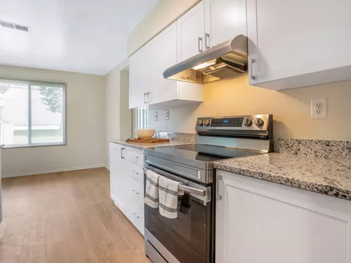 Renovated Package II kitchen featuring stainless steel appliances, white cabinetry, white speckled granite countertops, and hard surface flooring - eaves Tysons Corner