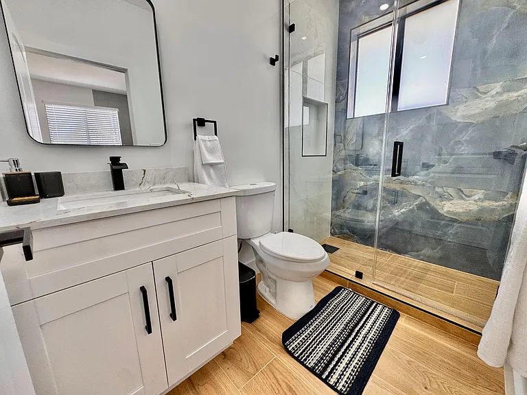 Updated bathroom with a wide vanity, matte-black fixtures, and a glass-enclosed shower with sleek tile surround.