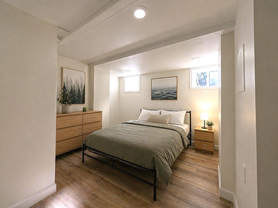 Furnished bedroom with a full bed, dresser and nightstand, plus wood-style floors and two windows for natural light.