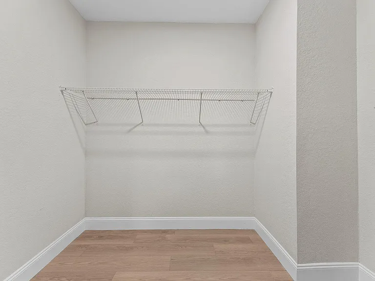 Dedicated walk-in closet with durable wood-look flooring and a full-length wire shelf for easy everyday storage.