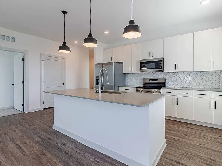 Open kitchen with a quartz island, stainless steel appliances, white cabinetry, and a herringbone tile backsplash. Open kitchen with a quartz island, stainless steel appliances, white cabinetry, and a herringbone tile backsplash.