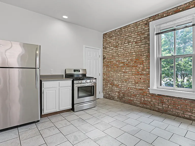 Kitchen view showcasing stainless steel appliances, gas range, exposed brick, and natural light