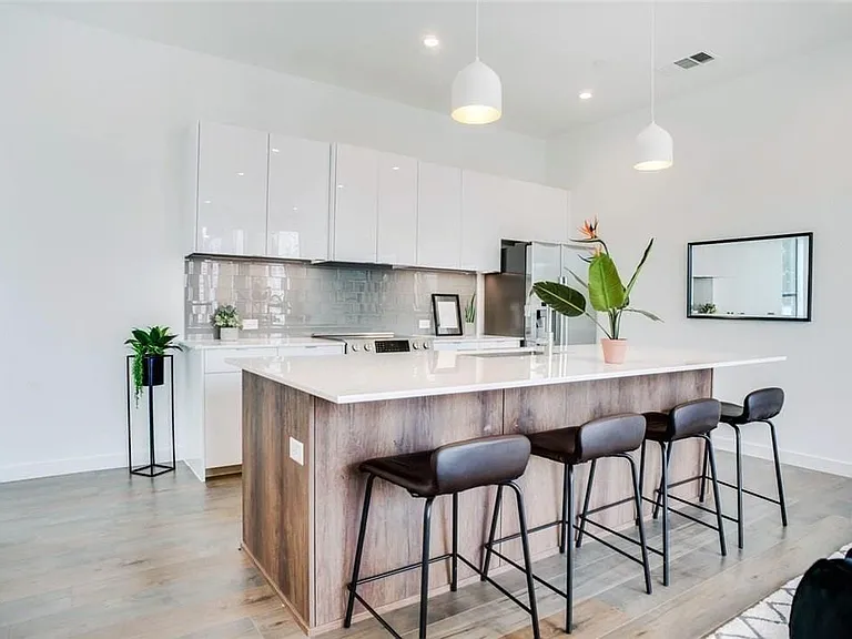 Modern kitchen featuring a large island with wood-finish paneling, white countertop, and pendant lighting