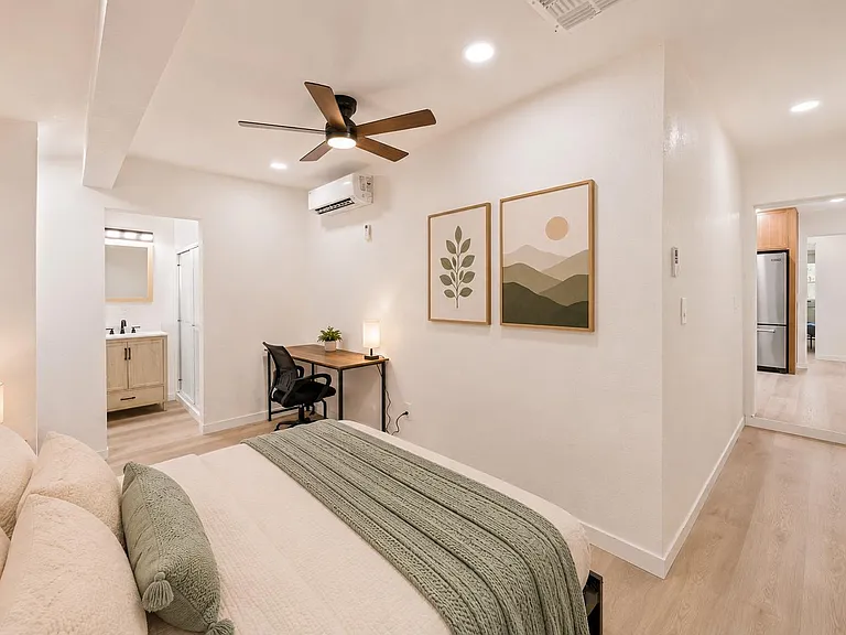 Spacious bedroom with a ceiling fan, dedicated desk area, and easy access to a nearby vanity and kitchen.