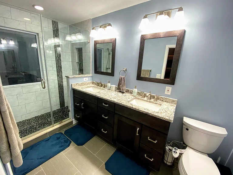 Fully renovated custom master bathroom with walk-in river rock shower, recessed storage, tile floor, double sinks, granite countertops, spacious cabinets and custom vanity with backlit mirror.