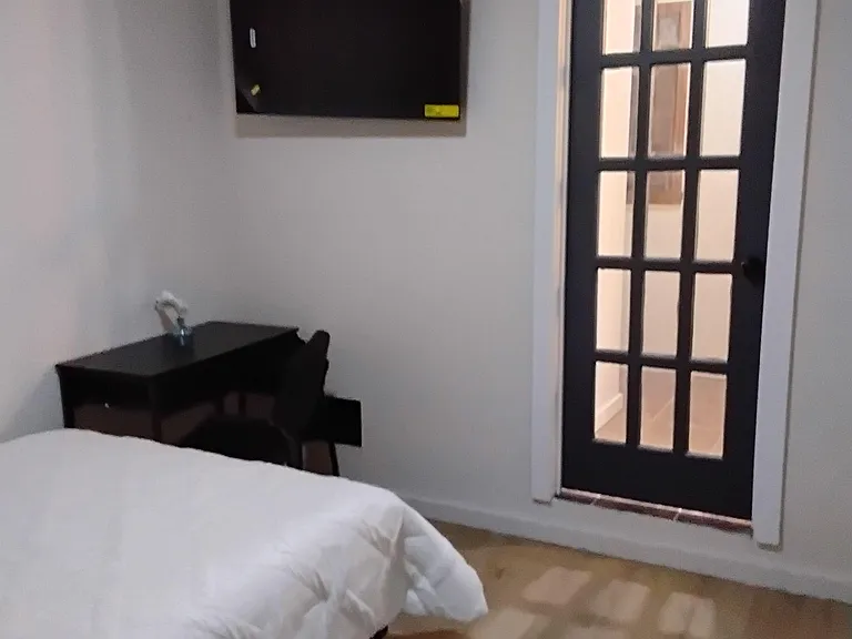Furnished bedroom with a bed, wall-mounted TV, and a glass-paneled door for easy access to nearby common areas.
