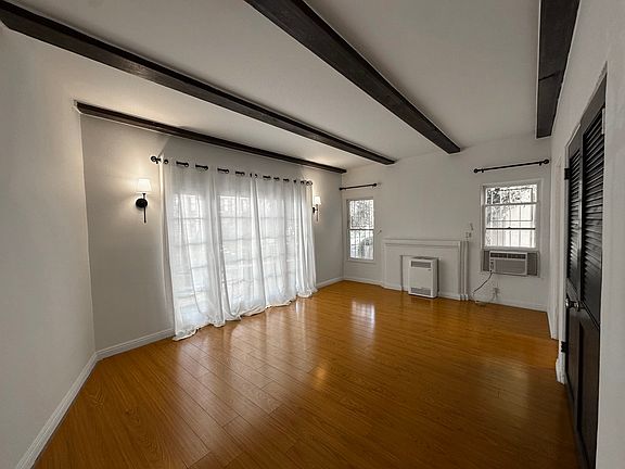 The living room is bright and spacious, featuring elegant beamed ceilings and large French windows that flood the space with natural light. Classic hardwood-style floors add warmth and charm, while the open layout provides a cozy yet airy atmosphere.
