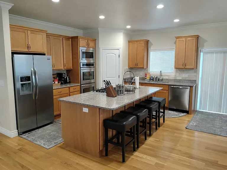 The fully furnished kitchen boasts a double oven, gas range, toaster, coffee station, spices, pots, pans, utensils, and sharp knives. It includes ample empty cupboard space for storage, providing everything you need for a seamless cooking experience.