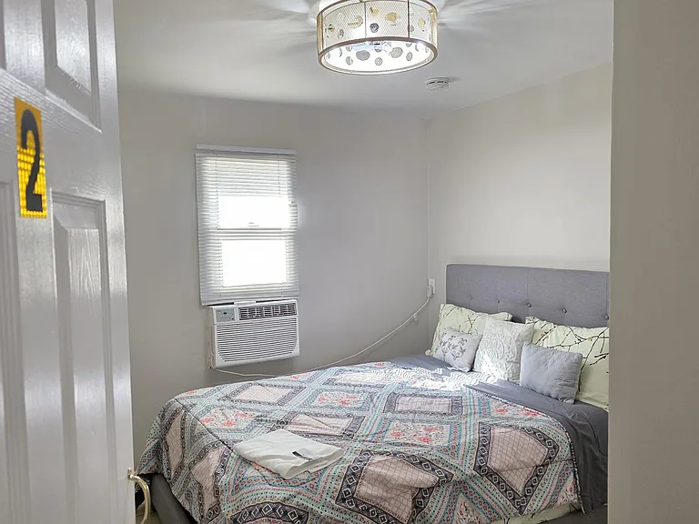 Private bedroom with a full bed, window blinds, and a ceiling light, plus a window A/C unit for in-room comfort.